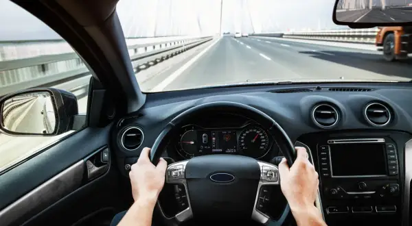 Ręce na kierownicy, jadąc przez most. Prędkościomierz pokazuje 130 km/h.
