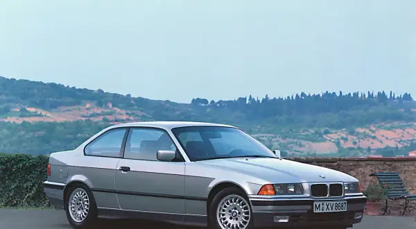 Srebrne BMW E36 coupe, idealne auto do driftu, stoi na tle malowniczego krajobrazu Toskanii.