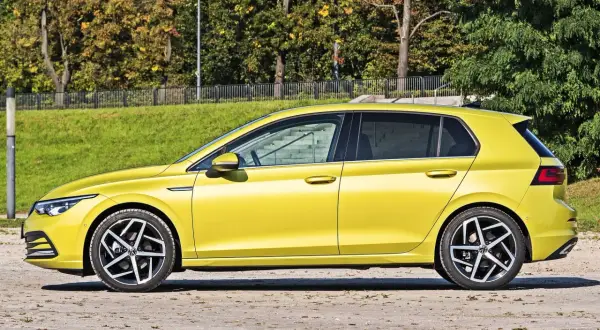 Żółty hatchback, czyli samochód z podnoszoną tylną klapą, zaparkowany na tle zieleni i drzew.