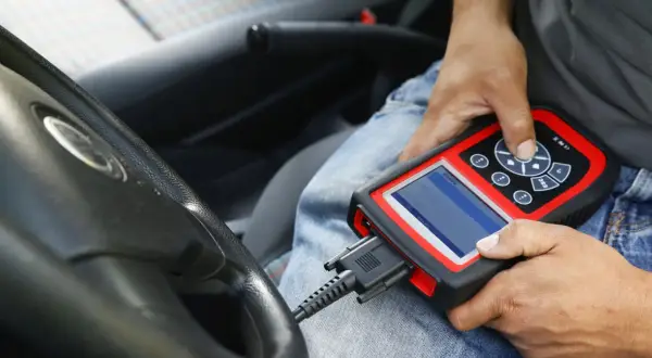 Diagnostyka komputerowa samochodu: mechanik podłącza skaner do złącza OBD w aucie, by sprawdzić jego stan techniczny.