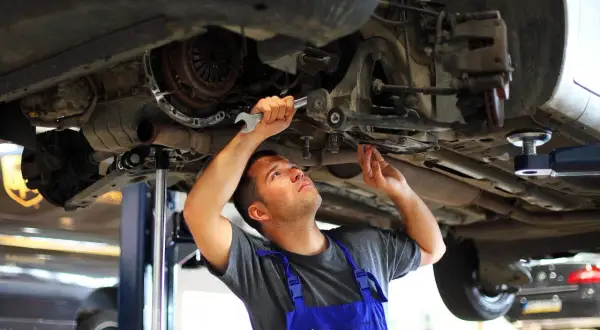 Mechanik wykonuje wymianę tulei wahacza domowym sposobem, używając klucza do precyzyjnej pracy.