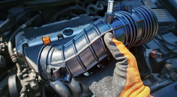 Ręka w rękawicy trzyma element układu dolotowego silnika 1.8T. Może to być związane z objawami zatkanej odmy.