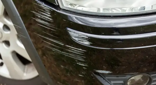 Widoczne liczne rysy na czarnym zderzaku plastikowym, wymagające naprawy.