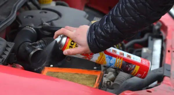 Ręka trzyma puszkę z preparatem samostart do diesla, rozpylając go w pobliżu filtra powietrza w silniku samochodu.