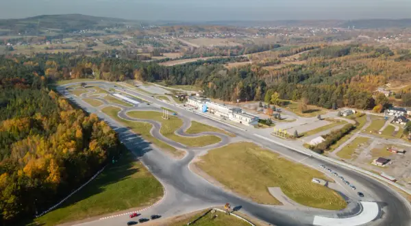 Widok z lotu ptaka na tor wyścigowy Kielce otoczony jesiennymi lasami. Kilka samochodów na torze.