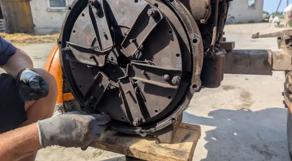 Mechanik w rękawiczkach reguluje mechanizm sprzęgła, przygotowując traktor do pracy.