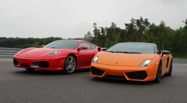 Czerwone Ferrari i pomarańczowe Lamborghini stoją obok siebie na torze wyścigowym, gotowe do rywalizacji.