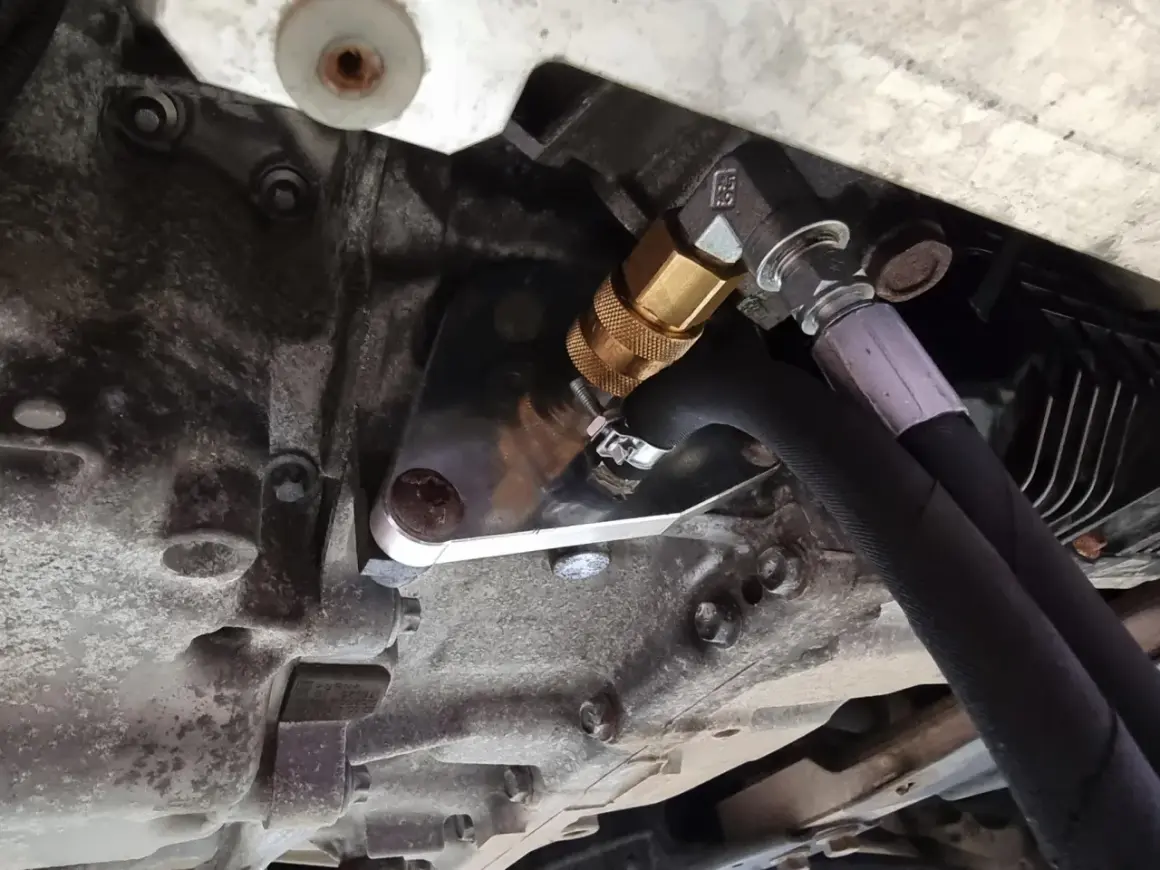 Metalowy adapter z szybkozłączką do dynamicznej wymiany oleju w skrzyni biegów, podłączony do węży.