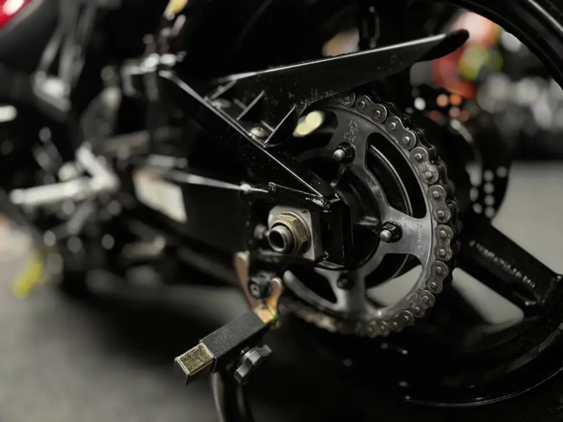 Zbliżenie na tylne koło motocykla z widocznym łańcuchem i zębatką, gotowe do czyszczenia łańcucha motocyklowego.