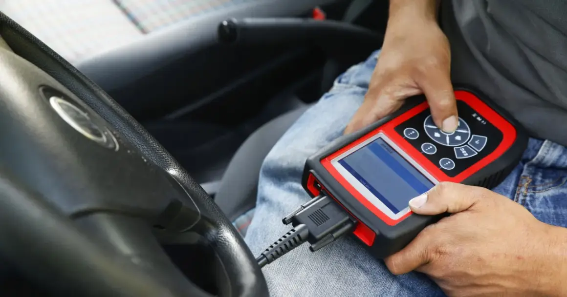 Diagnostyka komputerowa samochodu: mechanik podłącza skaner do złącza OBD w aucie, by sprawdzić jego stan techniczny.