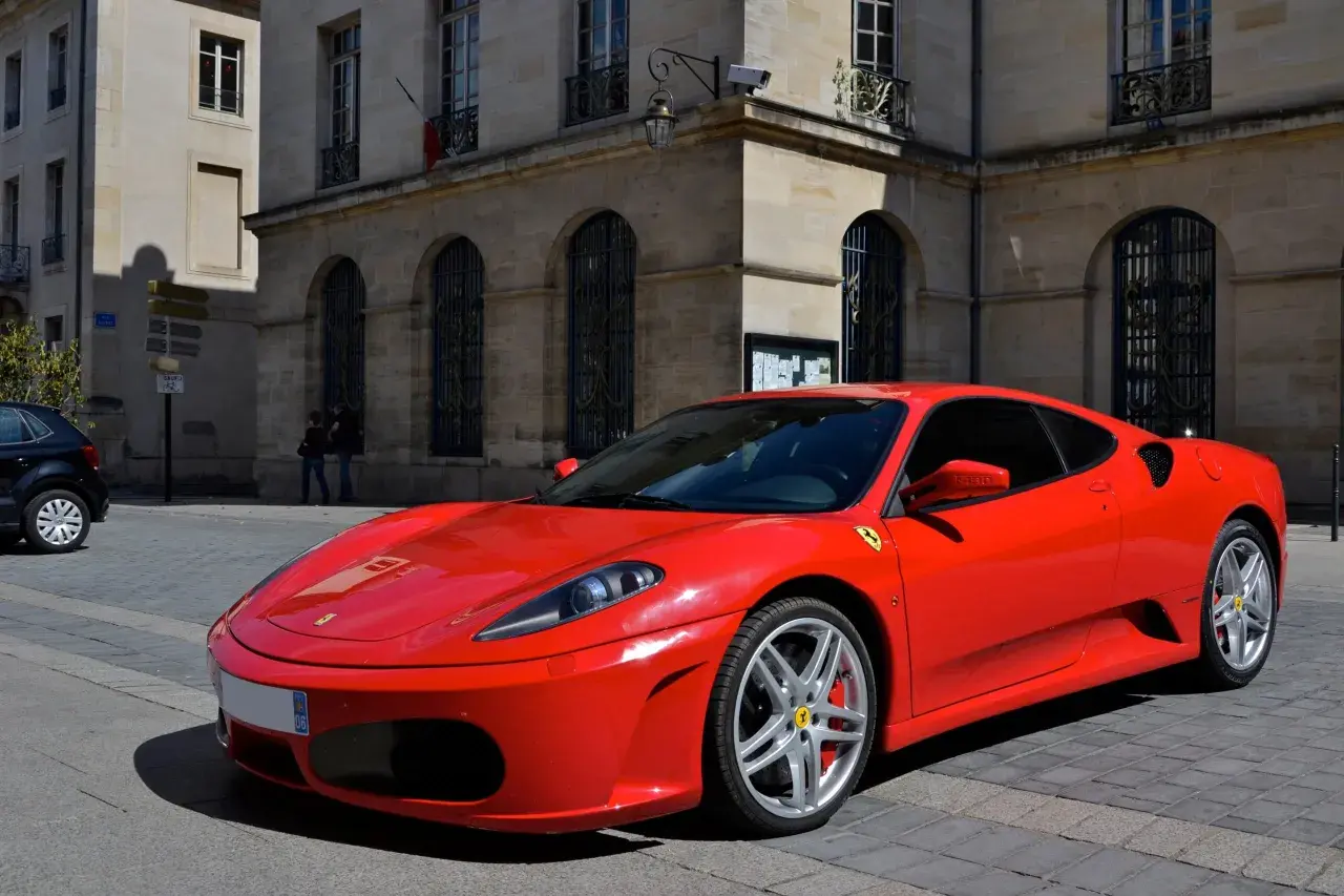 Czerwone włoskie auto sportowe Ferrari F430 na brukowanej ulicy przed zabytkową kamienicą.