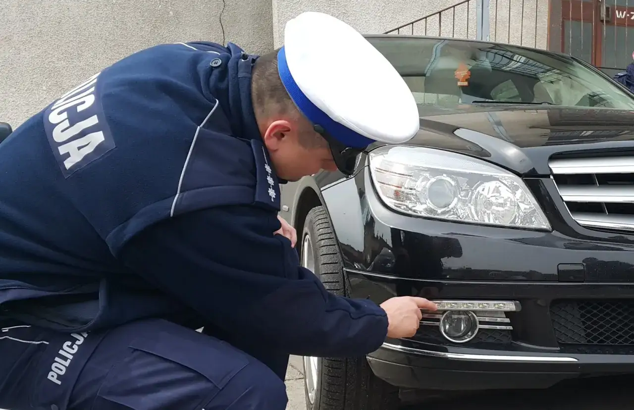 Policjant sprawdza, jakie światła do jazdy w dzień zamontowano w czarnym samochodzie.