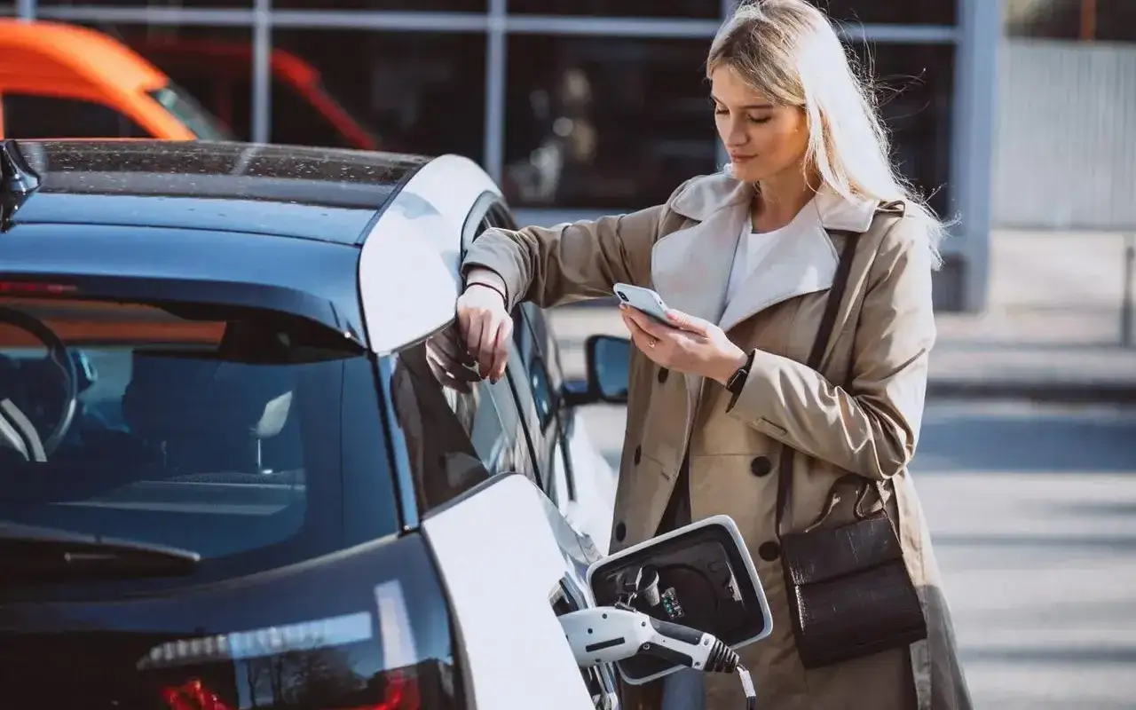 Kobieta ładuje samochód elektryczny, zastanawiając się nad wadami i zaletami silnika hybrydowego.