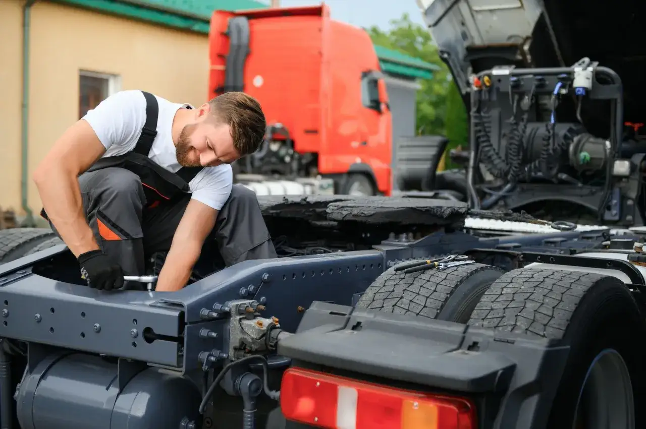 Mechanik naprawia ciężarówkę, sprawdzając uszkodzony wahacz. Objawy mogą być różne, od nierównego zużycia opon po problemy z kierowaniem.