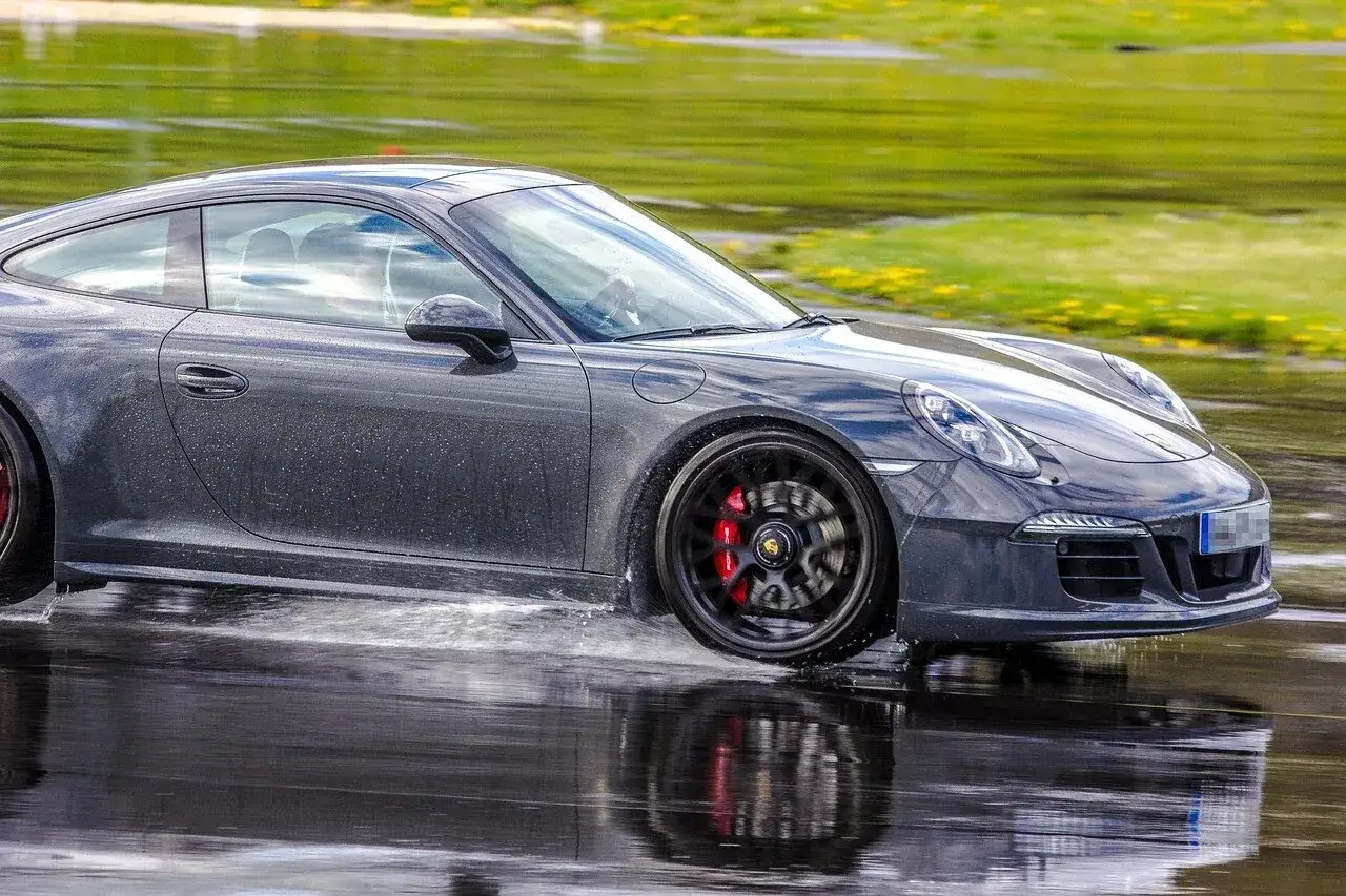 Szary Porsche z napędem RWD (tylny napęd) śmiga po mokrej nawierzchni, rozpryskując wodę.