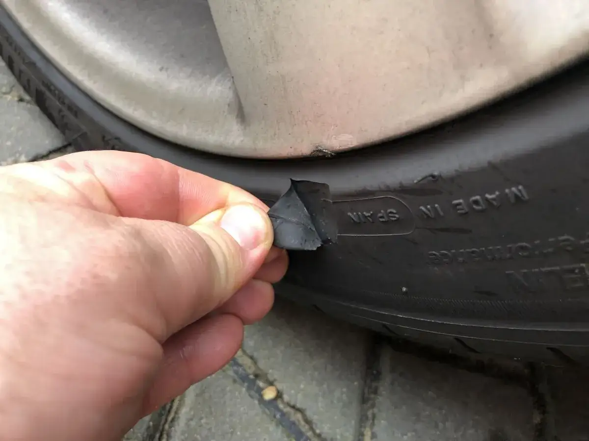 Dłoń sprawdza uszkodzenie boku opony, które może wymagać naprawy.