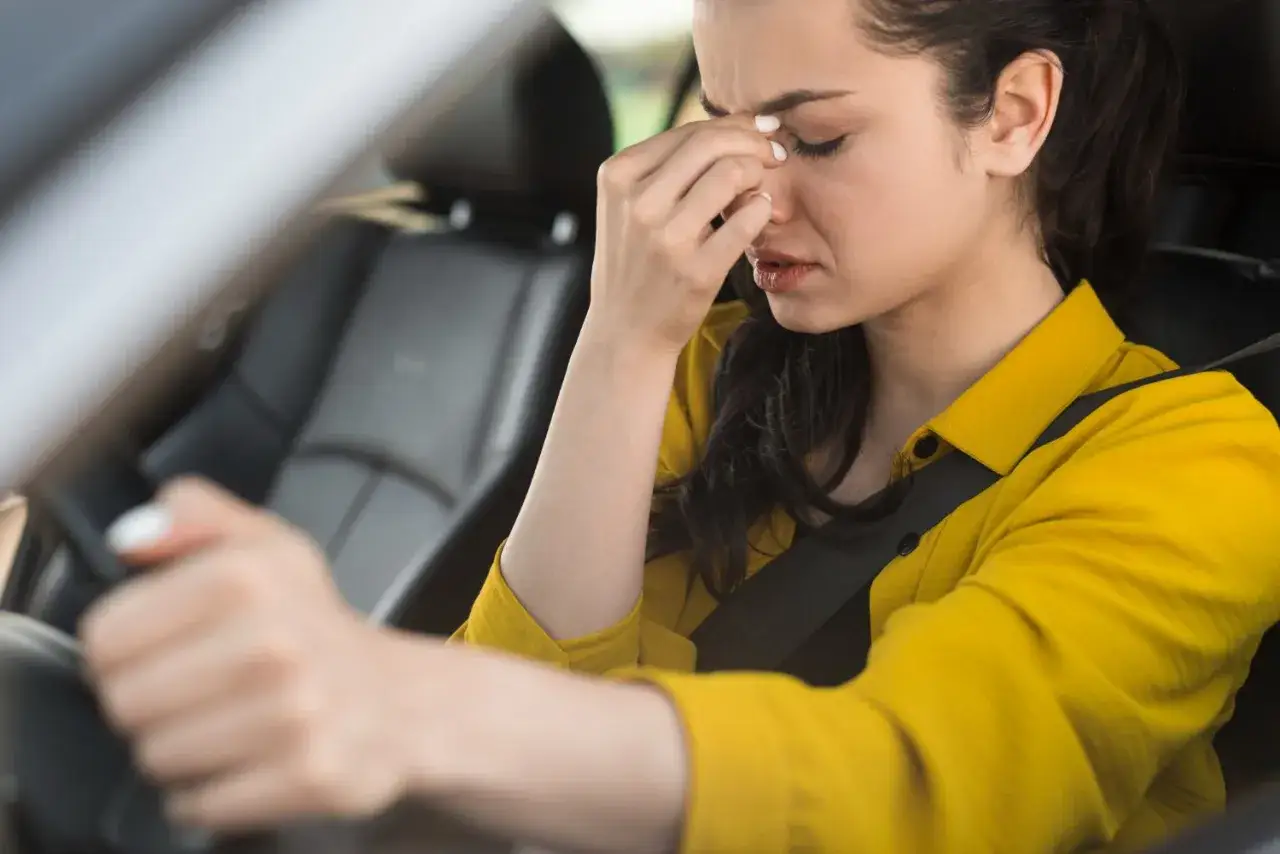 Kobieta w żółtej koszuli siedzi za kierownicą, masując skronie. Wciskam gaz, a auto nie przyspiesza, co doprowadza ją do frustracji.