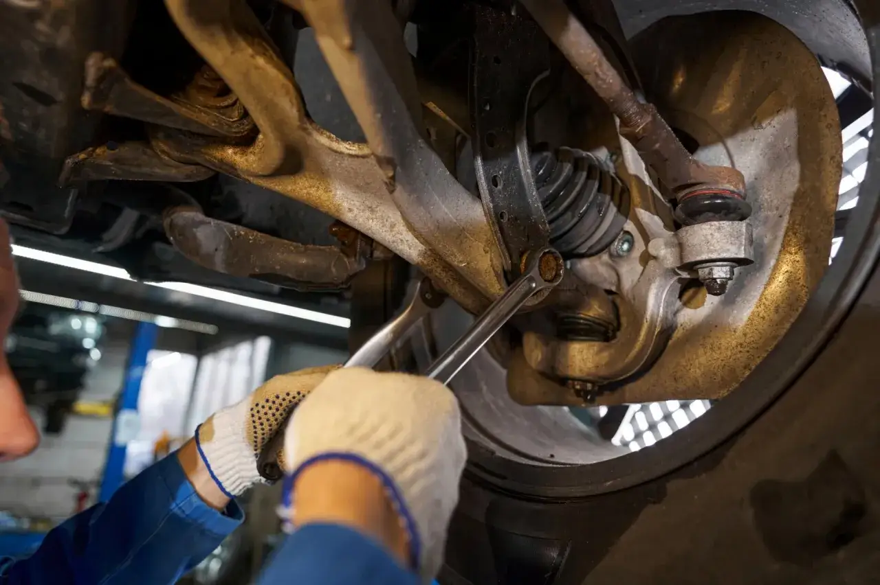 Mechanik w rękawiczkach dokręca śrubę w zawieszeniu samochodu, by wyeliminować stuki w zawieszeniu.
