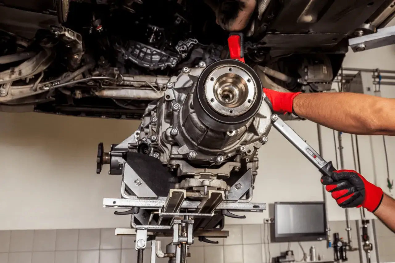 Mechanik w czerwonych rękawicach dokonuje wymiany skrzyni biegów w samochodzie na podnośniku.