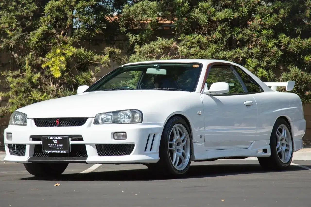 Biały Nissan Skyline R34 z charakterystycznym spoilerem i felgami, gotowy do jazdy.