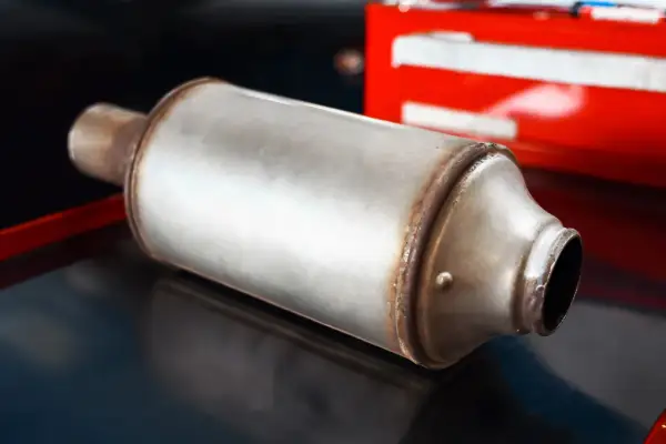 Metalowy tłumik, element układu wydechowego, prawdopodobnie dpf w benzynie, leży na ciemnym tle.