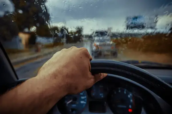 Deszczowa pogoda, ręka na kierownicy, a auto nie odpala. Widać deszcz na szybie i inne samochody w oddali.