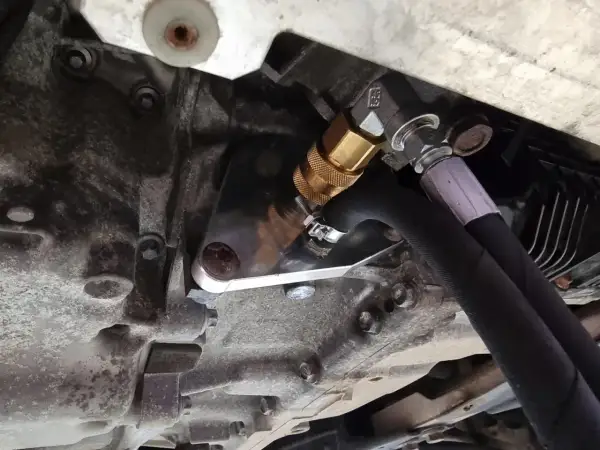 Metalowy adapter z szybkozłączką do dynamicznej wymiany oleju w skrzyni biegów, podłączony do węży.