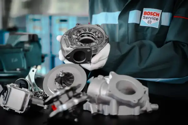 Mechanik w białych rękawiczkach prezentuje części turbosprężarki. Zwróć uwagę na uszkodzony wąż turbiny objawy, gdy widzisz takie elementy.