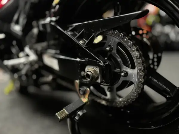 Zbliżenie na tylne koło motocykla z widocznym łańcuchem i zębatką, gotowe do czyszczenia łańcucha motocyklowego.