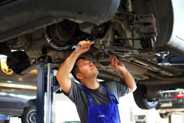 Mechanik wykonuje wymianę tulei wahacza domowym sposobem, używając klucza do precyzyjnej pracy.