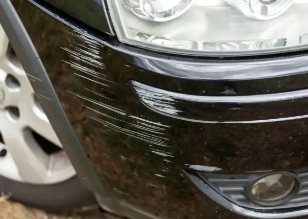 Widoczne liczne rysy na czarnym zderzaku plastikowym, wymagające naprawy.
