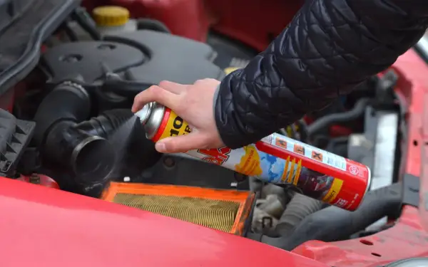 Ręka trzyma puszkę z preparatem samostart do diesla, rozpylając go w pobliżu filtra powietrza w silniku samochodu.